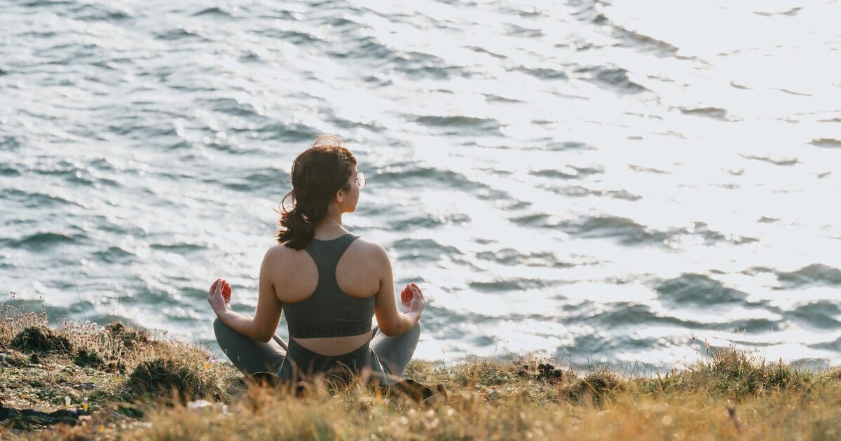 Woman meditating on the rocks near a beach.